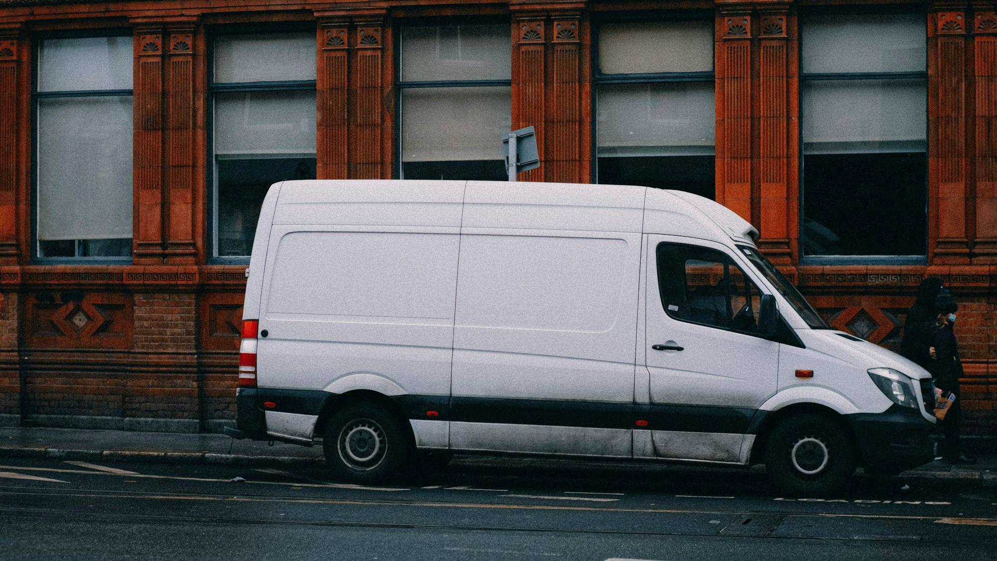 A white Sprinter cargo van parked on a city street in front of a brick building